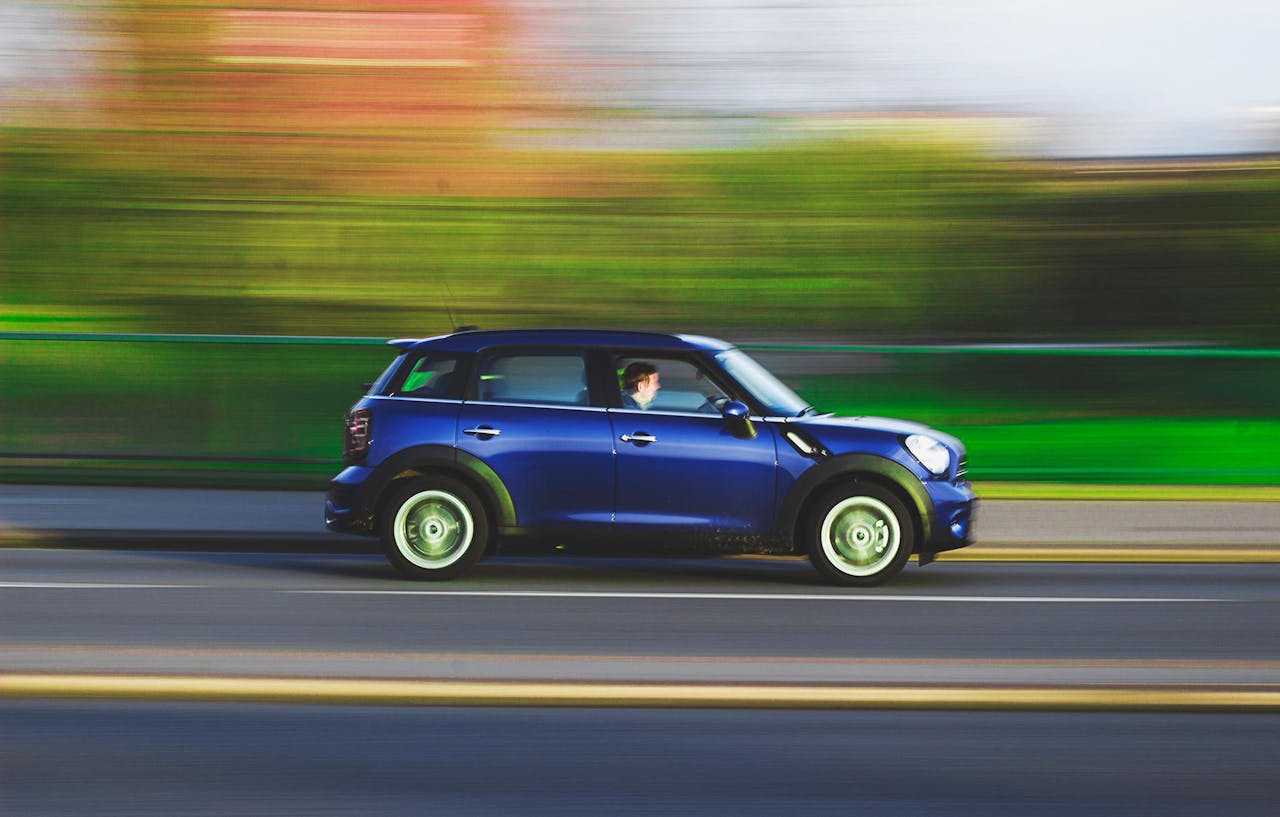 A blue car swiftly drives on a road with a blurred background, capturing speed and movement.